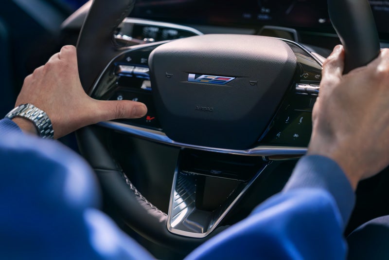 Close-up of a Man About to Press the V-Button on the 2026 OPTIQ-V Steering Wheel | Palmen Cadillac in Kenosha WI